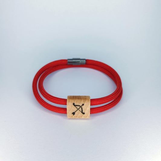 A red paracord bracelet with a square light wood charm engraved with a black bow and arrow symbol, resting on a light gray background.